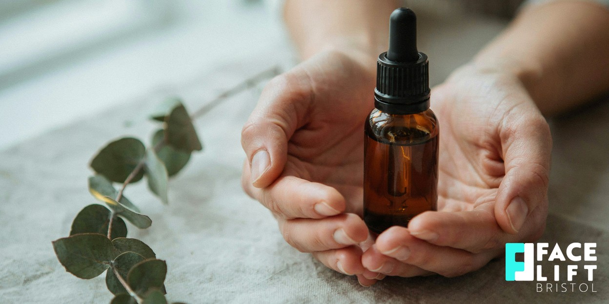 Close-up of a person’s hands gently holding a small amber glass skincare bottle in warm natural daylight, conveying calm aftercare and self-care