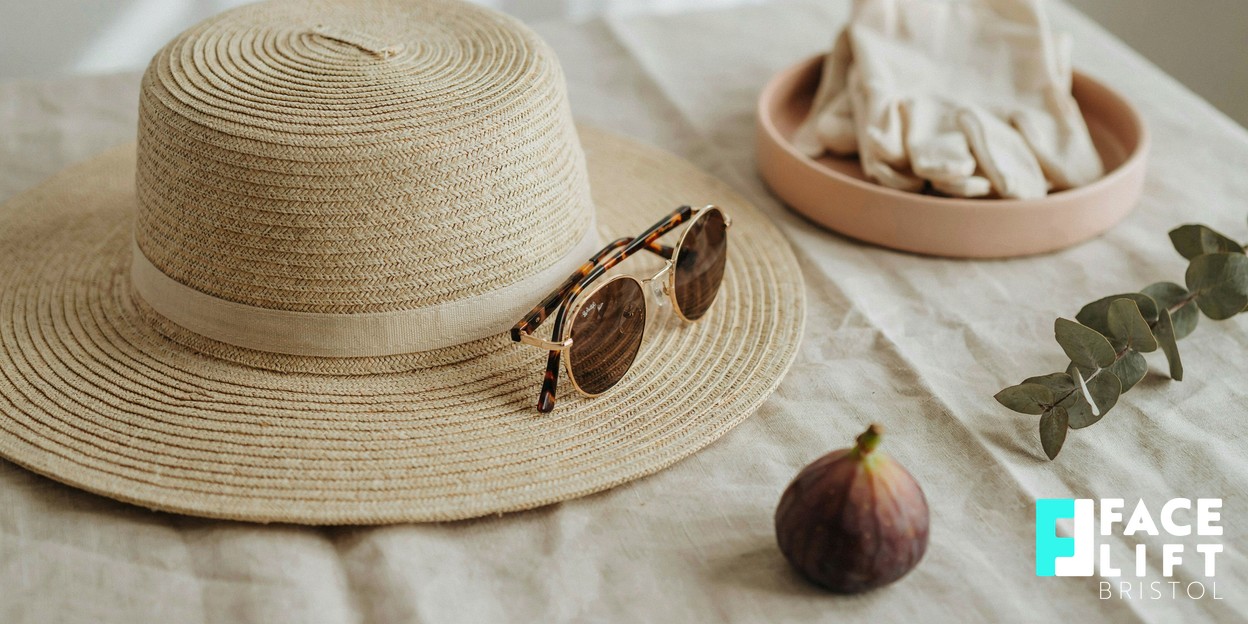 Calm still-life of a wide-brimmed straw sun hat and a pair of sunglasses resting on soft linen in bright natural daylight, evoking everyday sun protection