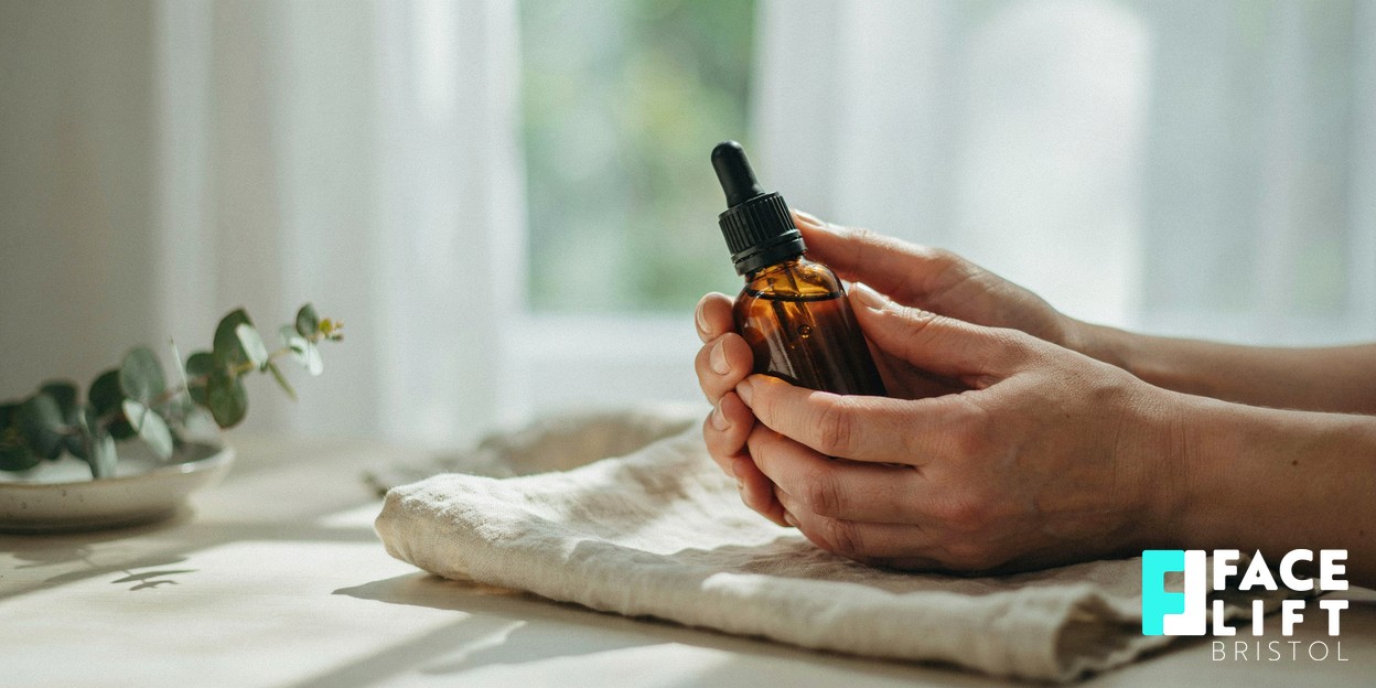 Close-up of a person’s hands cradling a small unbranded glass skincare bottle in soft daylight, conveying calm, considered aftercare