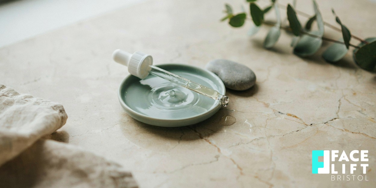 Photorealistic still life of a clear glass dropper resting beside a small dish of water with soft ripples, on a pale stone surface in gentle daylight, evoking pure regenerative skin science
