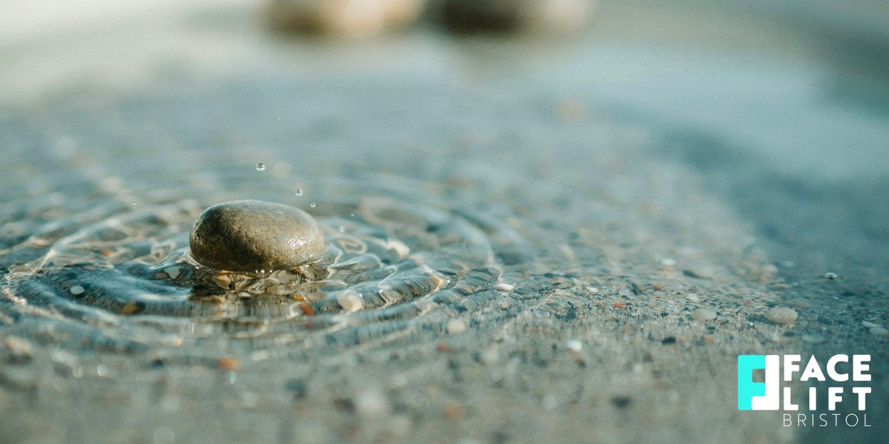 Still-life of a smooth polished pebble resting on rippling water in soft daylight, symbolising calm, hydration and renewal