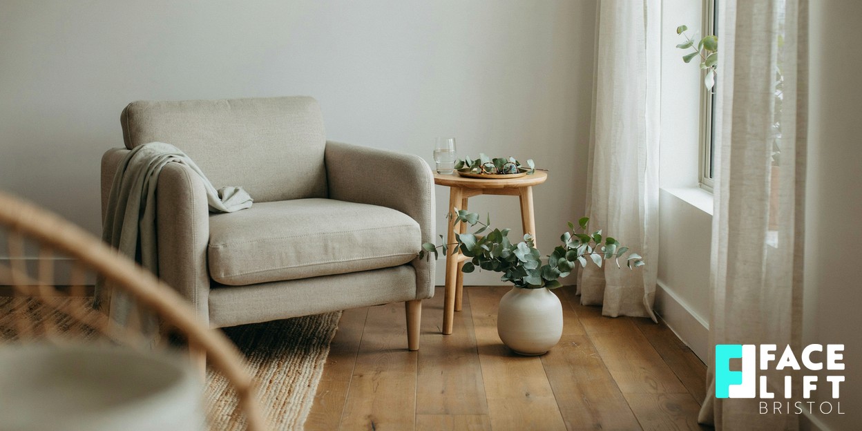 A calm, softly lit modern consultation room with a linen chair, a window with sheer curtains and a small vase of greenery, suggesting an unhurried professional discussion
